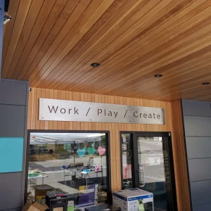 A metal panel with the words work, play, create cut out installed above doors to a business