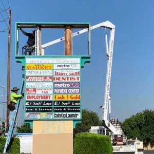 two sign installers changing signage for a business on a bucket truck and a ladder